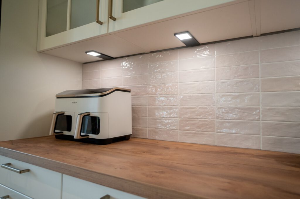 Moderne Küchenecke mit Holzarbeitsplatte, weißem Küchengerät und beige glänzenden Wandfliesen.