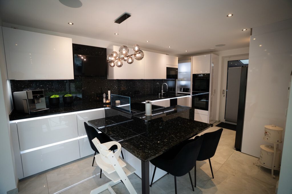 Moderne, aufgeräumte Küche mit weißen Hochglanzschränken, schwarzen Granitarbeitsplatten und stilvollen Details.
