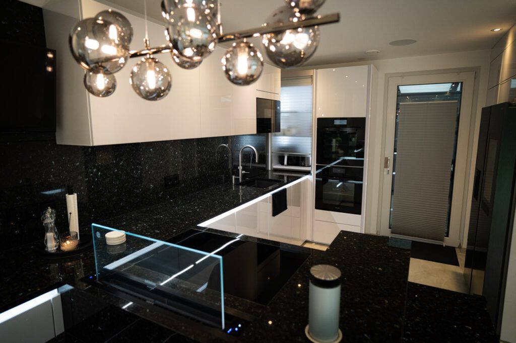 Moderne, stilvolle Küche mit schwarzer Granitinsel, glänzenden Oberflächen und eleganter Beleuchtung.