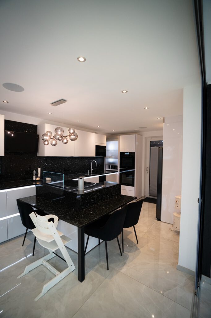 Moderne, minimalistische Küche mit schwarzem Küchenblock, weißen und schwarzen Stühlen, eleganten Geräten.