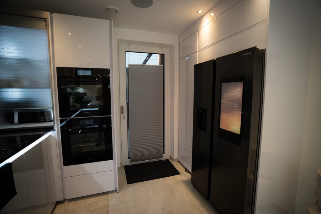 Moderne Küche mit schwarzem Kühlschrank, weißem Einbauschrank und Glastür mit Plissee-Rollo.