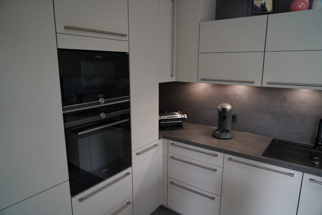 Moderne, minimalistische Küche mit weißen Schränken, Einbaugeräten und schwarzen Akzenten.