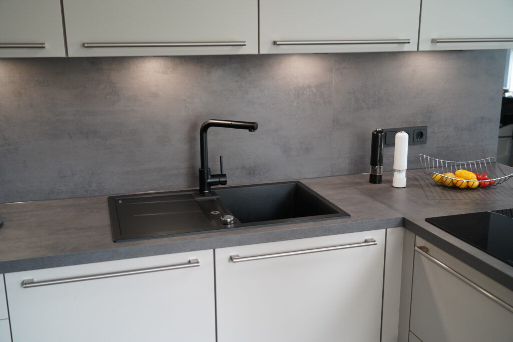 Moderne Küche mit grauer Arbeitsplatte, schwarzem Wasserhahn und Obstschale mit Zitronen und Tomaten.