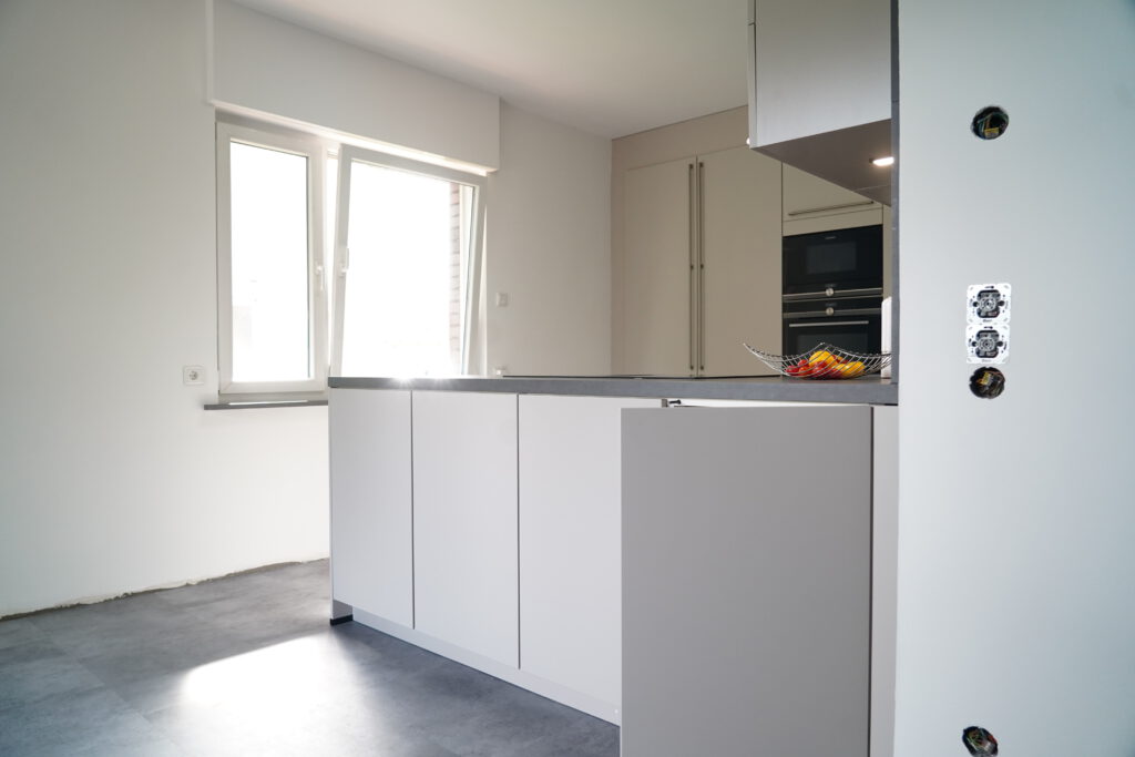 Moderne, helle Küche mit weißer Kücheninsel, grauer Arbeitsplatte und bunter Obstschale.