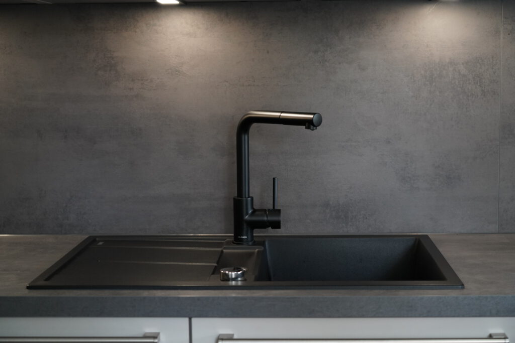 Moderne schwarze Küchenspüle mit minimalistischem Wasserhahn auf dunkler, eleganter Arbeitsplatte.