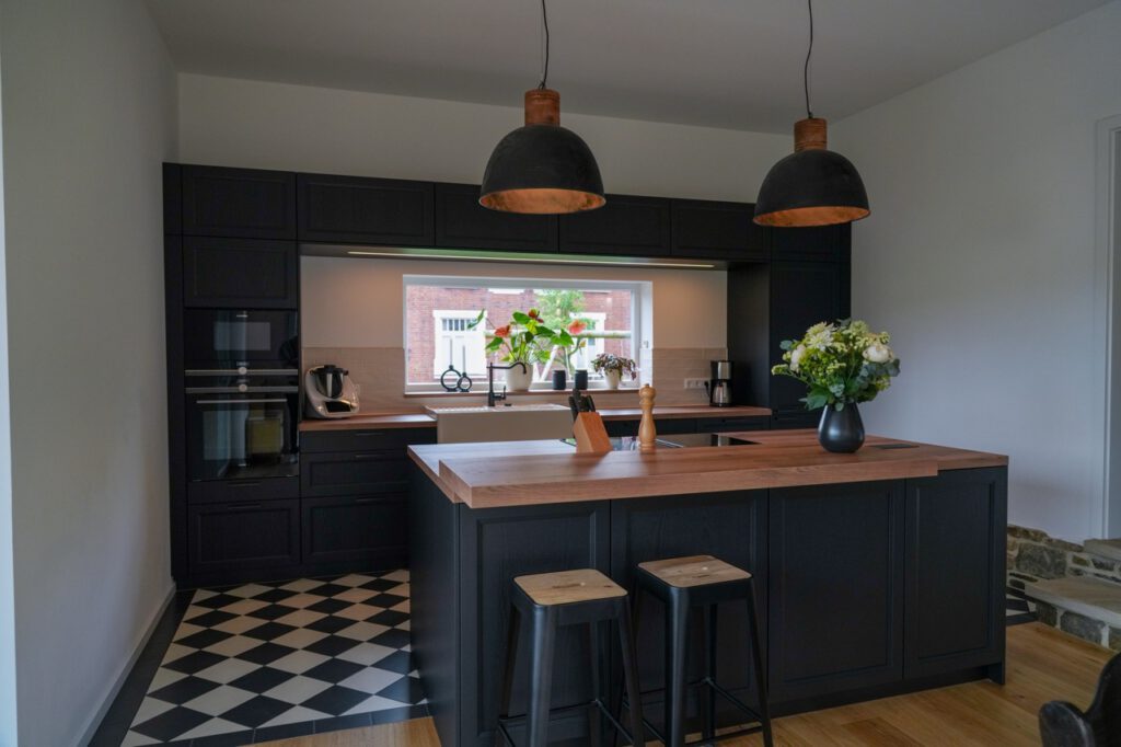 Moderne Küche mit schwarzer Kücheninsel, Holzarbeitsplatte, Hockern und eleganten Hängeleuchten.