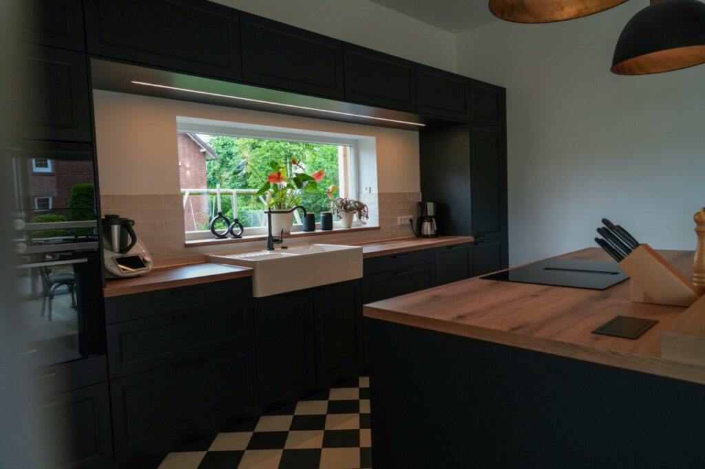 Moderne Küche mit dunklen Schränken, Holzarbeitsplatten, großen Fenstern und Pflanzen.