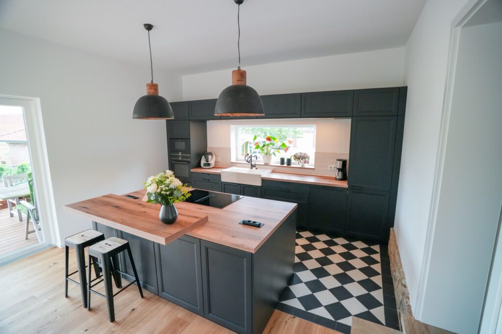 Moderne Küche mit Holzarbeitsplatte, dunklen Schränken, großem Fenster und stilvollen Barhockern.