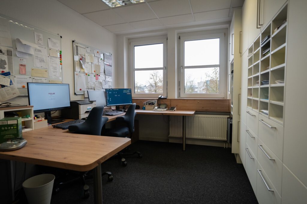 Ein ordentliches Büro mit zwei Schreibtischen, Computern, Bürostühlen und einem großen Aktenschrank.