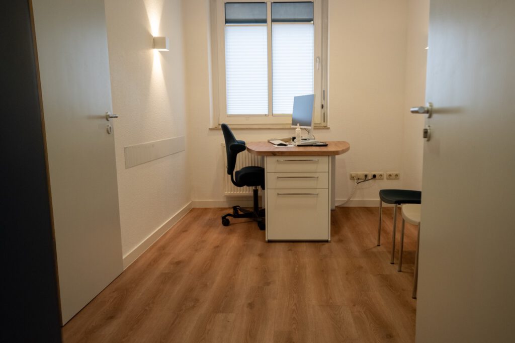 Ein schlichtes Büro mit Schreibtisch, Computer, Bürostuhl und Fenster; bereit für den nächsten Besucher.