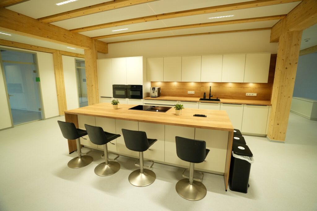 Moderne, minimalistische Küche mit Holzinsel, schwarzen Barhockern und weißen Schränken.
