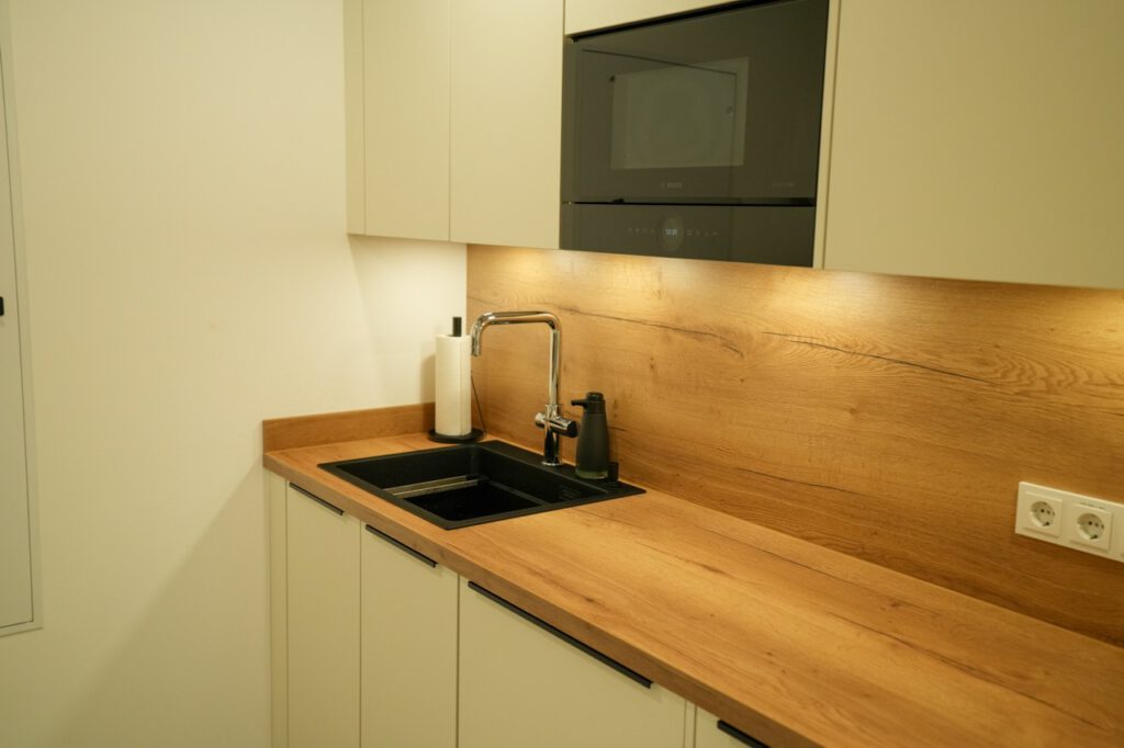 Moderne Küchenecke mit Holzarbeitsplatte, schwarzer Spüle und hellen Schränken, minimalistisch gestaltet.