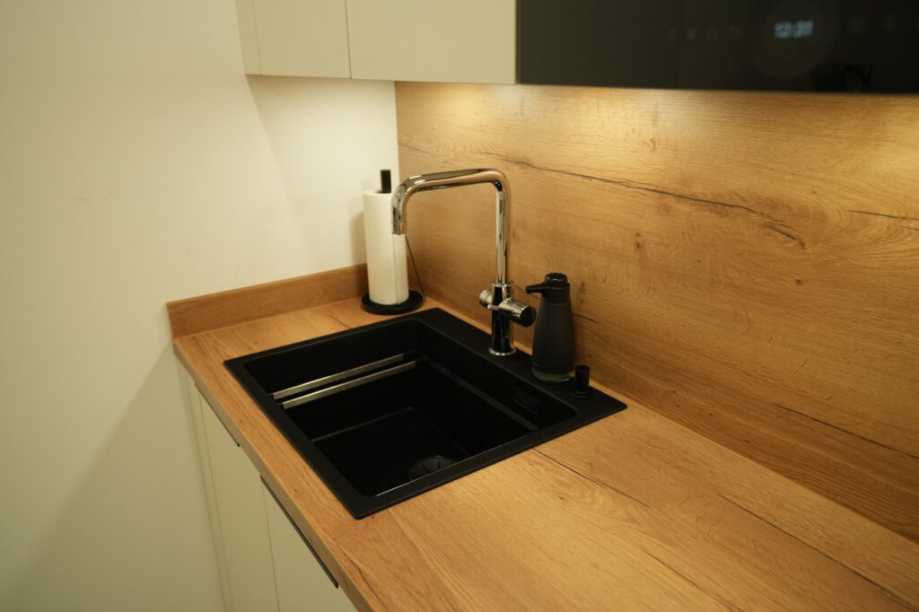 Moderne Küchenecke mit schwarzem Waschbecken, silbernem Wasserhahn und hellem Holzspritzschutz.
