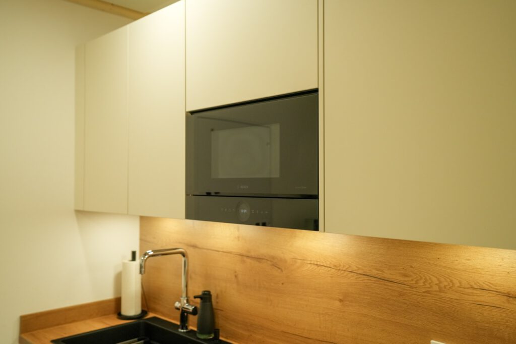 Moderne Küche mit hellem Schrank, Holzarbeitsplatte, schwarzem Backofen und Waschbecken.