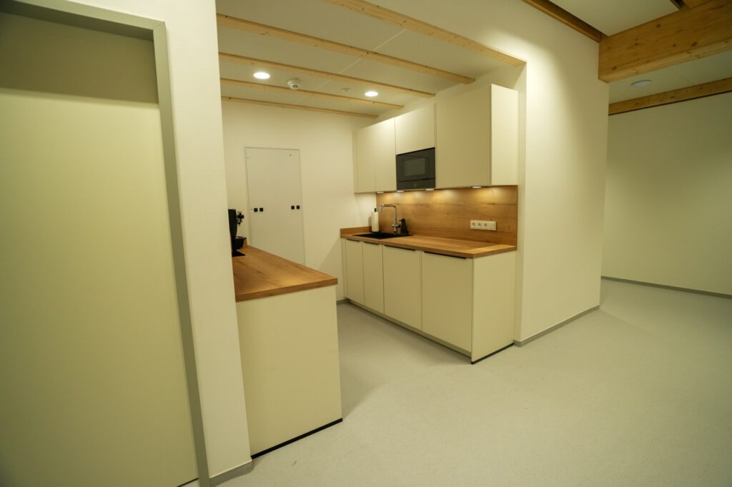 Moderne, minimalistische Küche mit cremefarbenen Schränken, Holzarbeitsplatte und integrierter Mikrowelle.
