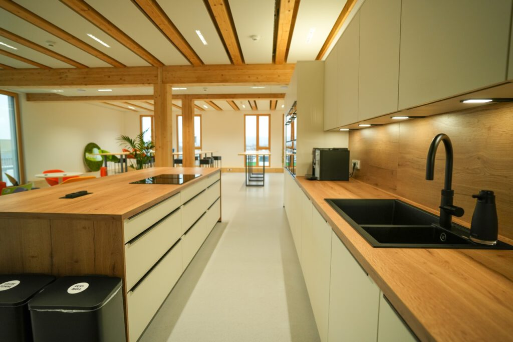 Moderne, aufgeräumte Küche mit Holz- und neutralen Tönen, ausgestattet mit Insel, Herd und Kaffeemaschine.