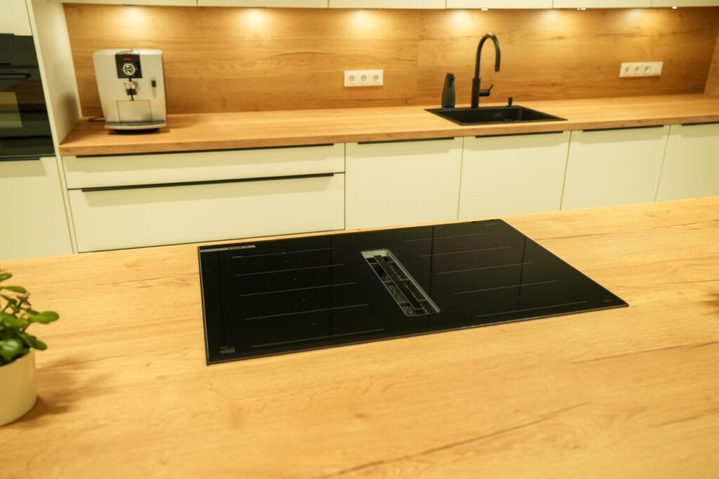 Moderne, minimalistische Küche mit Holzarbeitsflächen, Induktionskochfeld und weißen Schränken.