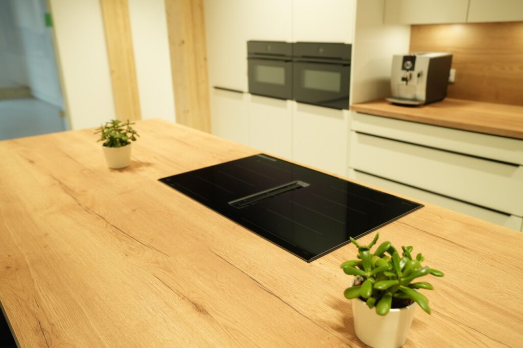 Moderne Küche mit Holztisch, Induktionskochfeld, weißen Schränken und grünen Pflanzen.