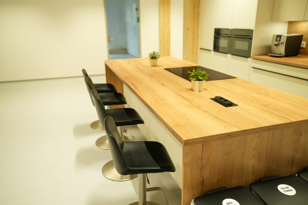 Moderne Küche mit Holzkücheninsel, schwarzen Barhockern, Pflanzen und eingebautem Kochfeld.