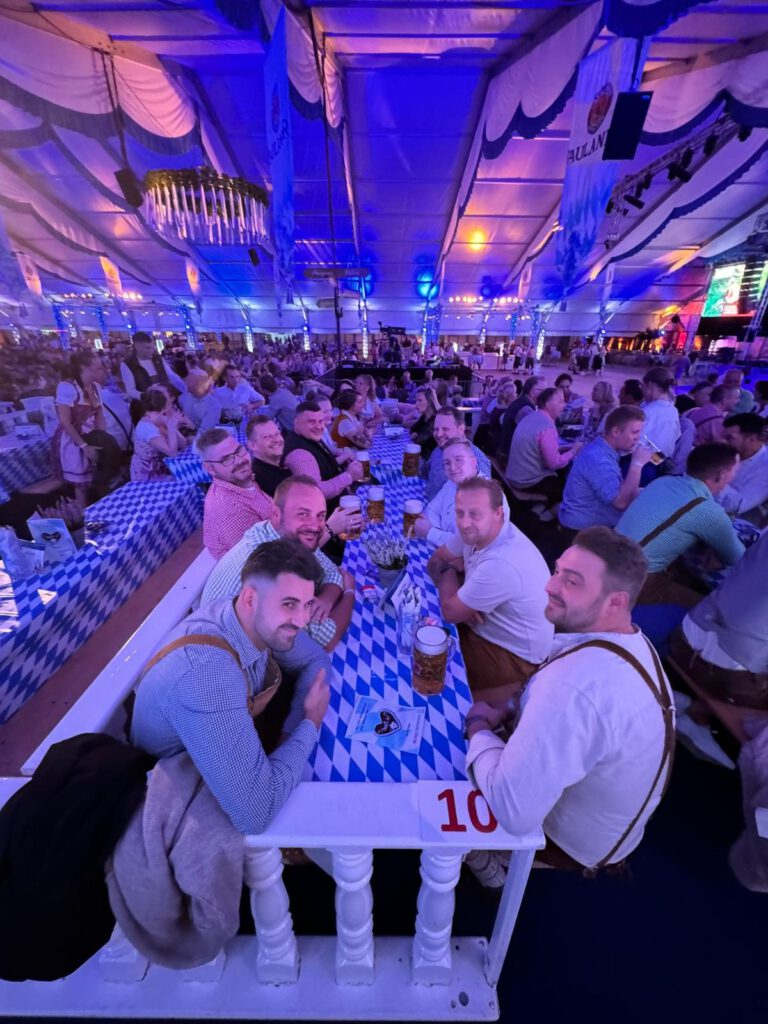 Menschen in bayerischer Tracht lachen und trinken Bier an einem festlich dekorierten Tisch im Festzelt.