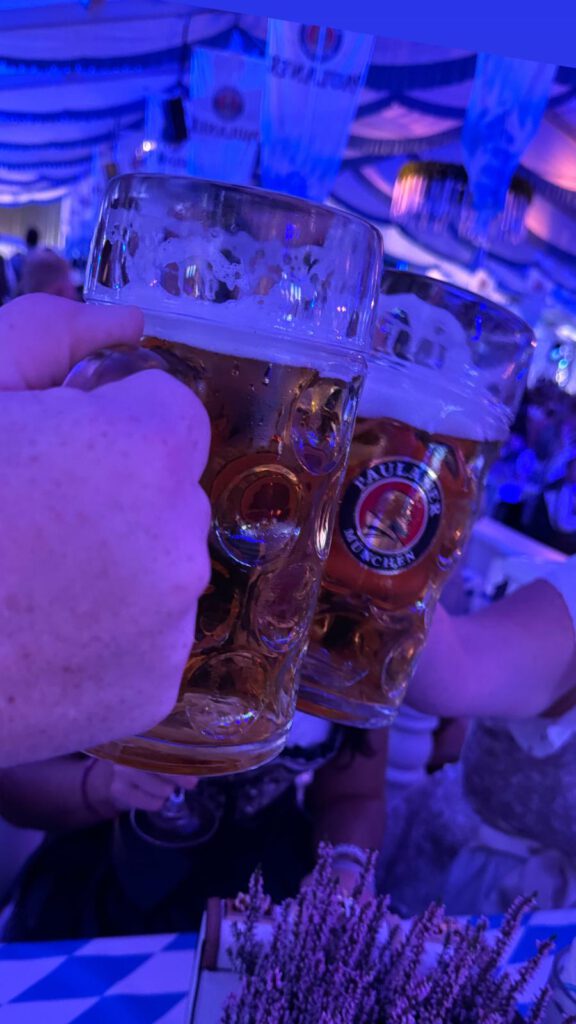 Zwei Personen stoßen auf einem bayerischen Fest mit großen Bierkrügen an, umgeben von festlicher Dekoration.