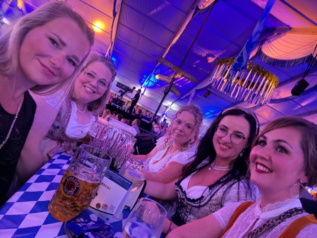Fünf Frauen in bayerischen Trachten sitzen fröhlich an einem Tisch mit Bierkrügen im Festzelt.