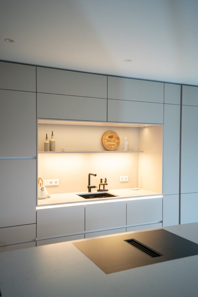 Moderne, minimalistische Küche mit hellen Schränken, Kochfeld, Spüle und dekorativen Elementen.