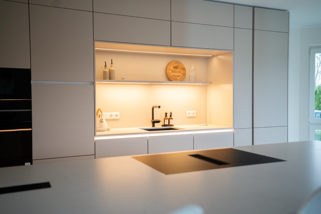 Moderne Küche in neutralen Tönen mit Einbauschränken, Waschbecken, Dekor und warmer Beleuchtung.
