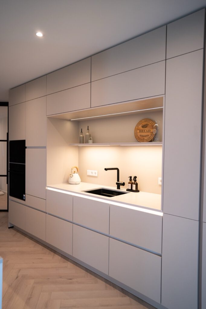 Moderne, minimalistische Küche mit heller Arbeitsplatte, schwarzem Wasserhahn und weißen Geräten.