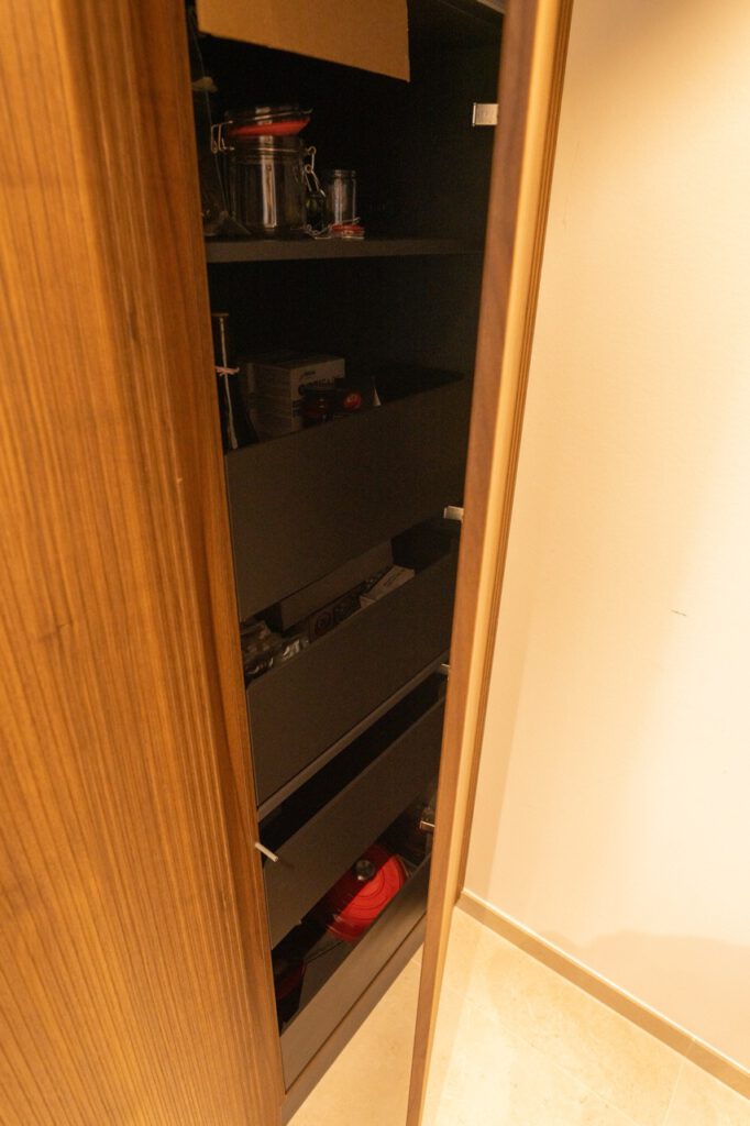 Offener Holzschrank mit Gläsern, Kartons und Haushaltsgegenständen in einer gemütlichen Umgebung.