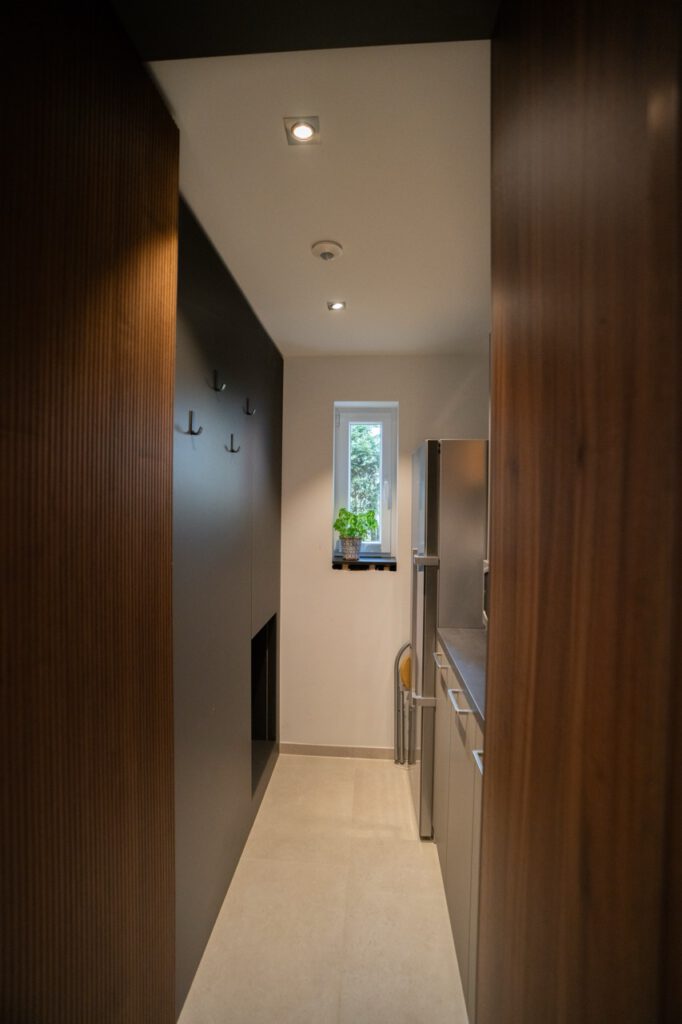 Moderner, schmaler Hauswirtschaftsraum mit Holzverkleidung, Pflanze auf Fensterbank und dunkler Wand.