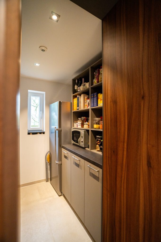 Gut organisierte Speisekammer mit silbernem Kühlschrank, Regalen voller Vorräte und einer Mikrowelle.