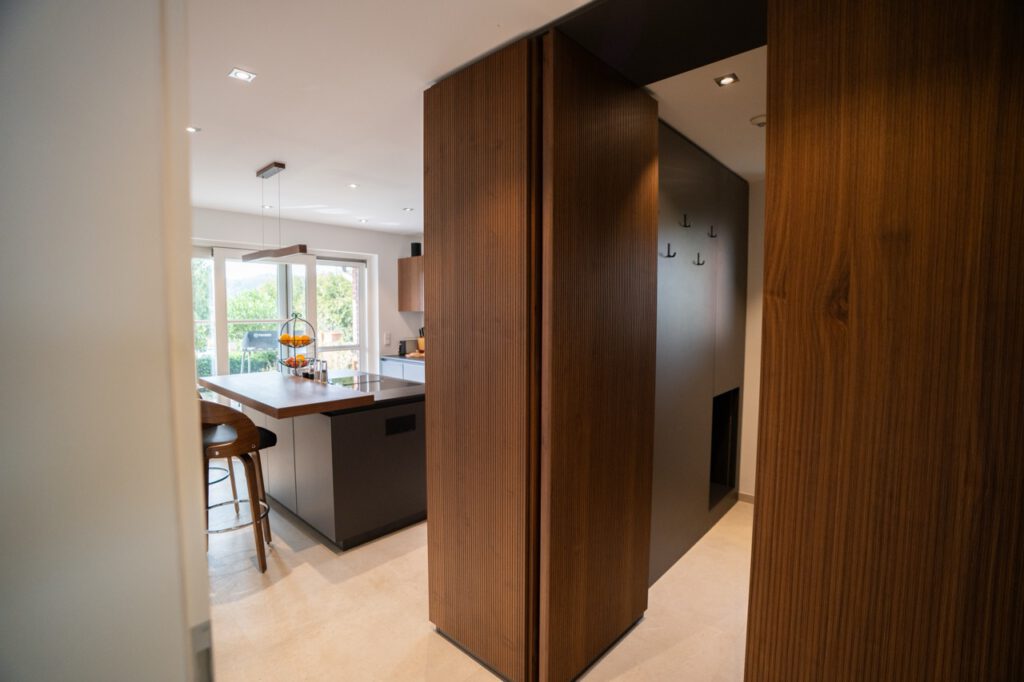 Moderne Küche mit Holztresen, Barhockern und viel natürlichem Licht durch ein großes Fenster.