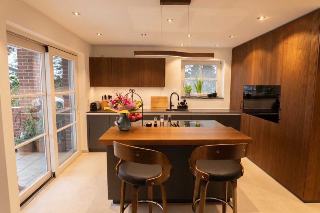 Moderne, einladende Küche mit Holzinsel, Barhockern, Blumenstrauß und eleganten Küchengeräten.