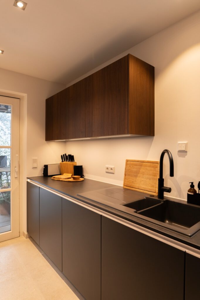 Moderne Küche mit dunklen Schränken, Holzdetails und eleganter Einrichtung in neutralen Tönen.