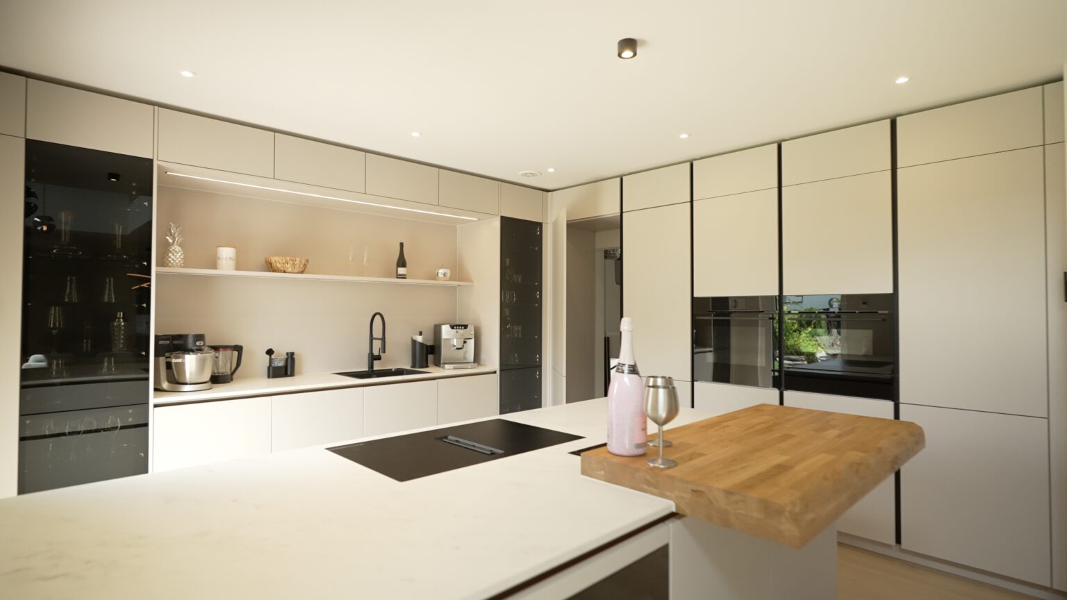 Moderne, minimalistische Küche mit weißer Insel, Holztheke, integrierten Geräten und dekorativen Elementen.