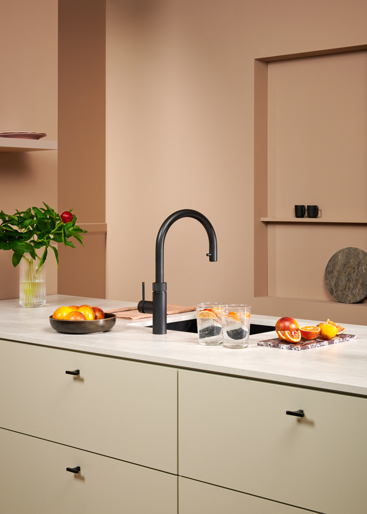 Moderne Küche mit schwarzem Wasserhahn, Zitrusfrüchten und grüner Vase auf heller Arbeitsplatte.