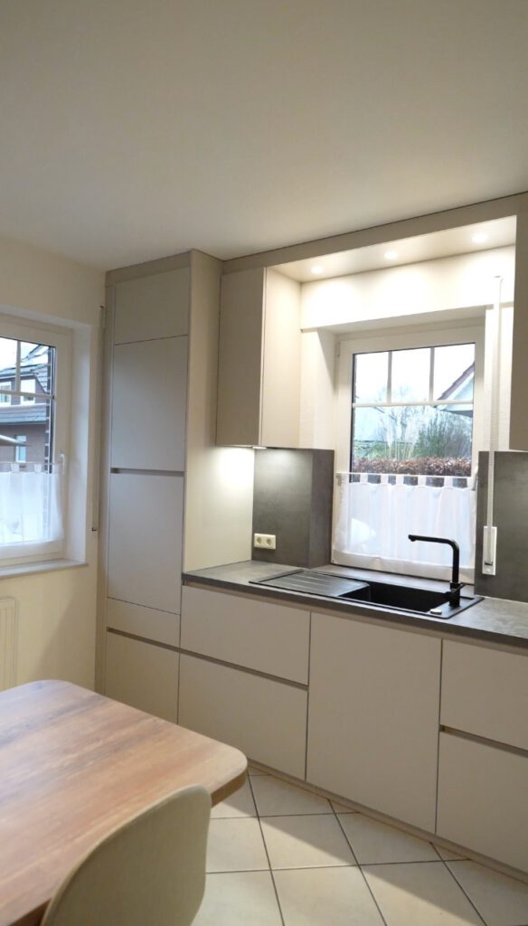 Moderne, minimalistische Küche mit hellen Schränken, dunkler Arbeitsfläche und Holz-Esstisch.