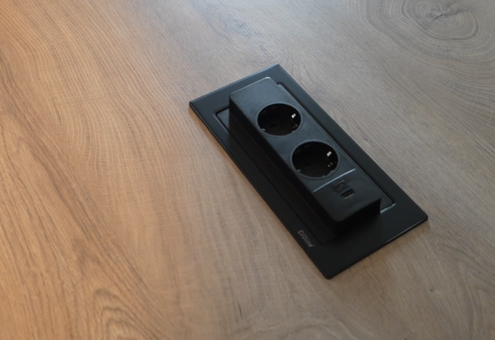 In einen Holztisch integrierte schwarze Steckdosenleiste mit USB-Anschlüssen, modernes Design.