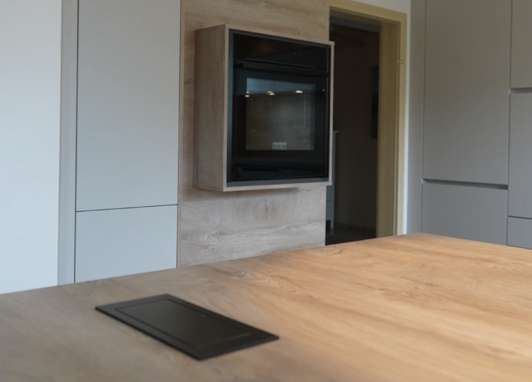 Moderne Küche mit Holzarbeitsplatte, grauen Schränken und eingebautem Backofen in Holzpaneel.
