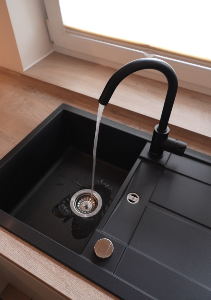 Moderne schwarze Küchenspüle mit fließendem Wasser, umgeben von einer warmen Holzarbeitsplatte.