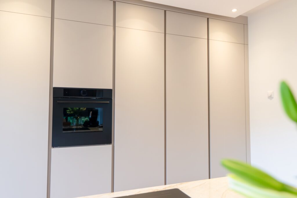 Moderne Küche mit hellen Schränken, schwarzem Backofen und Marmorarbeitsplatte, grüne Pflanze im Vordergrund.