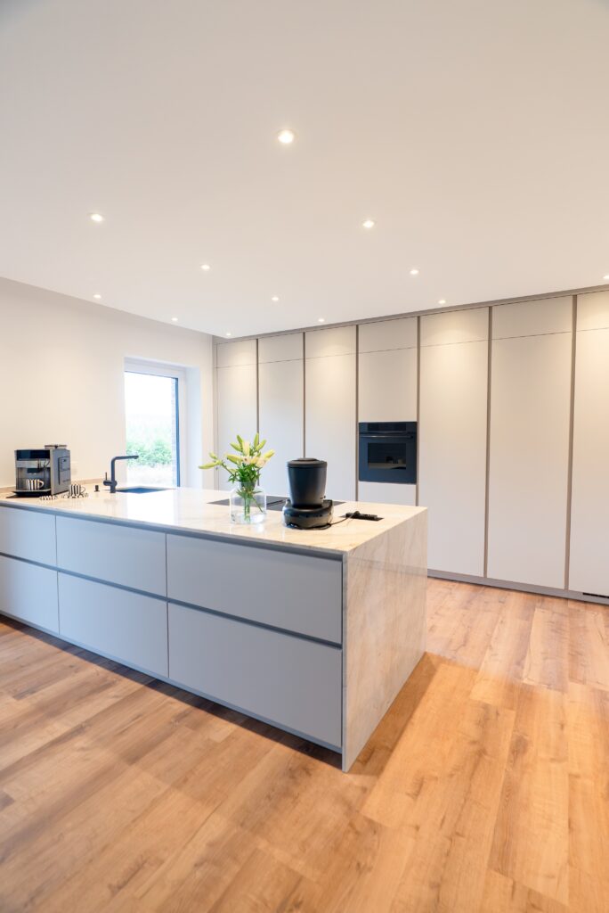 Moderne, minimalistische Küche mit großer Insel, Marmorarbeitsfläche, Blumen und Kaffeemaschine.