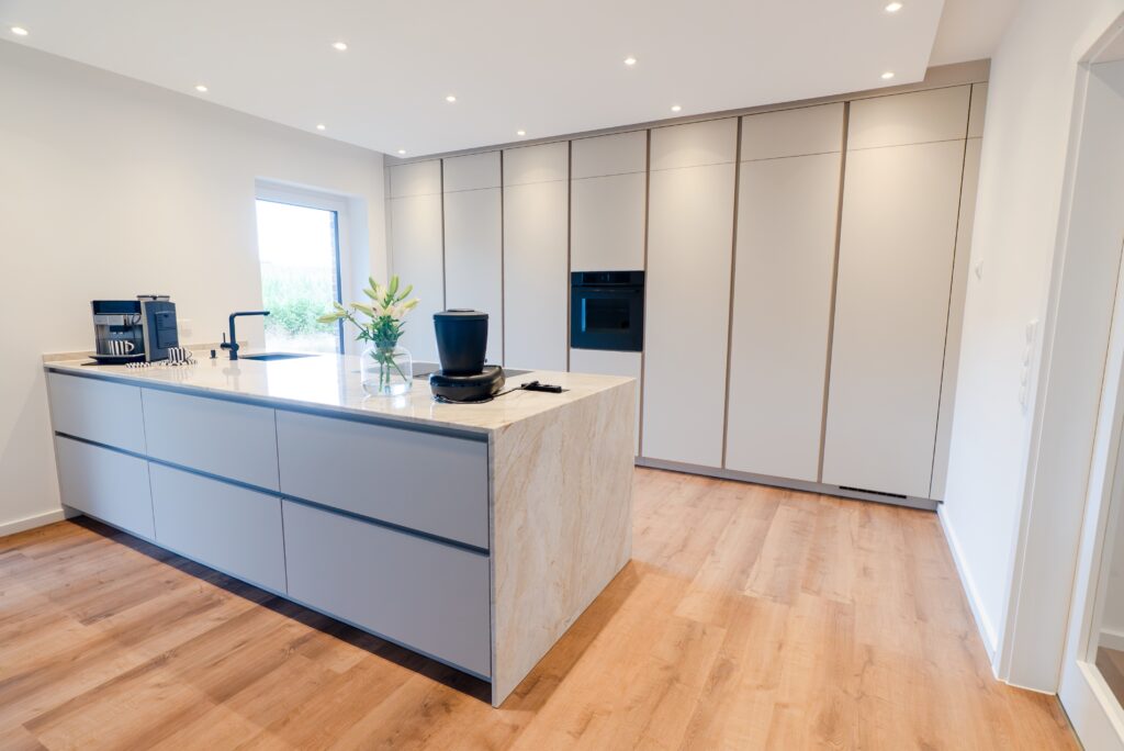 Moderne, minimalistische Küche mit großer Insel, Marmorplatte, Blumenstrauß und integriertem Backofen.