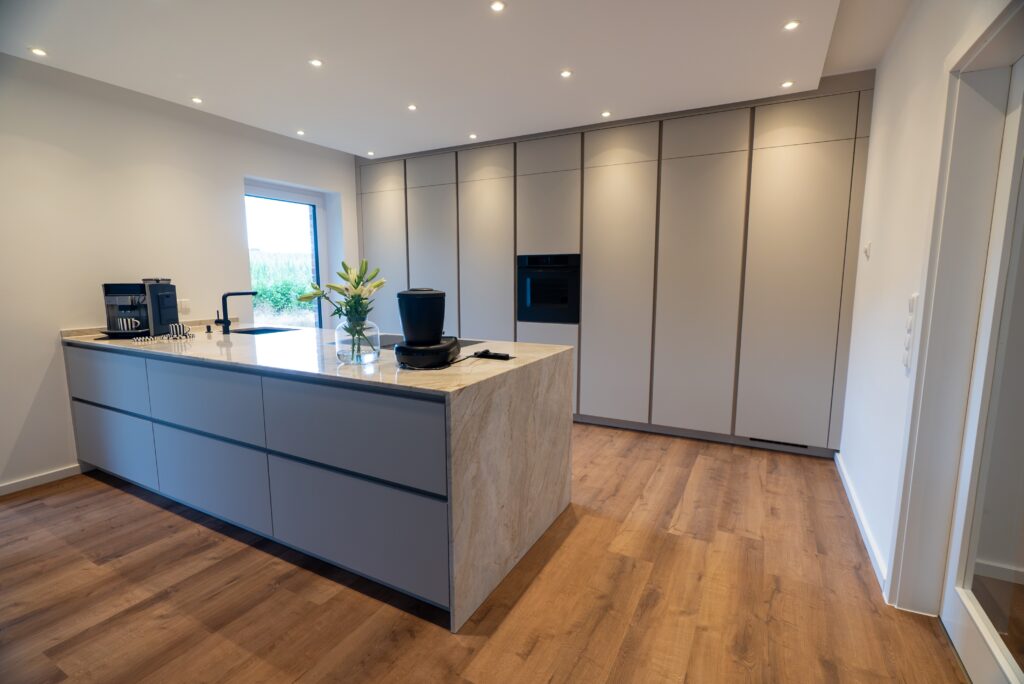 Moderne, minimalistische Küche mit heller Marmorinsel, Einbauschränken und natürlichem Licht.