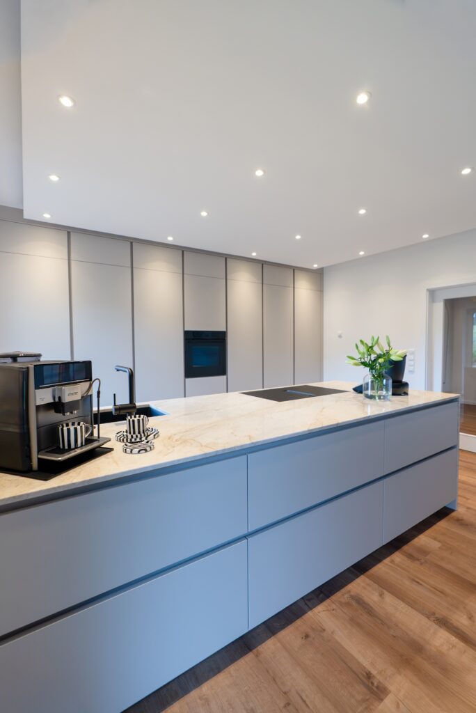 Moderne, minimalistische Küche mit heller Marmorinsel, Kaffeemaschine und Blumenstrauß.