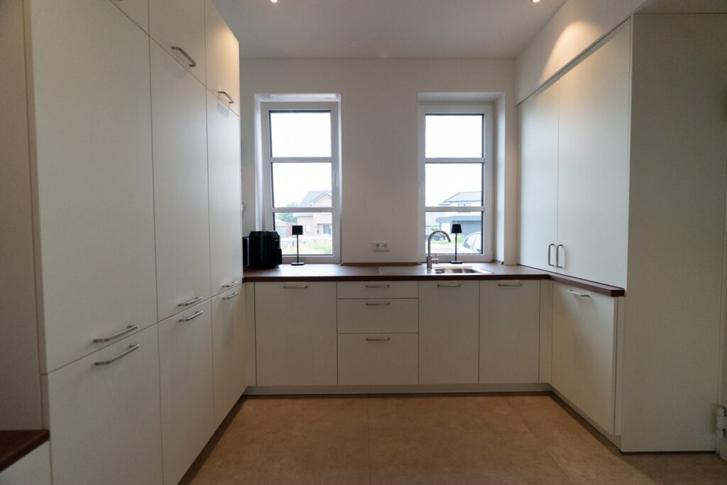 Moderne, minimalistische Küche mit weißen Schränken, dunkler Holzarbeitsplatte und natürlichem Licht.