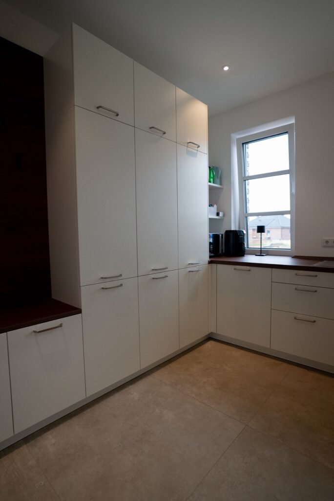 Moderne, helle Küche mit weißen Schränken, dunkler Arbeitsplatte und natürlichem Licht durch ein Fenster.