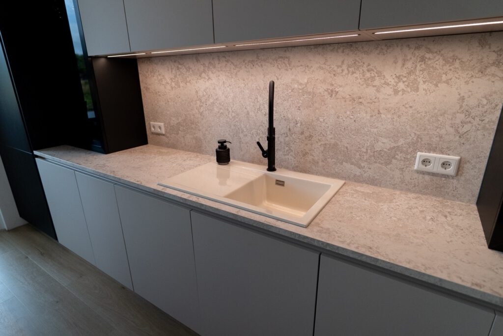 Moderne, minimalistische Küche mit grauer Marmorarbeitsplatte, schwarzem Wasserhahn und Beleuchtung.