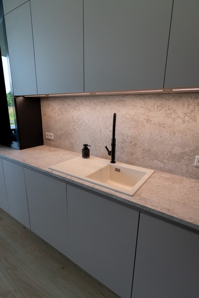 Moderne Küche mit grauen Schränken, steinartiger Arbeitsplatte und schwarzem Wasserhahn.